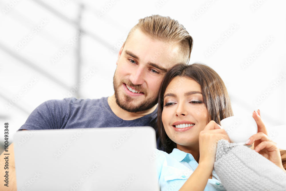 Happy couple sitting on sofa with coffee and working on a laptop Happy couple sitting on sofa with coffee and working on a laptop