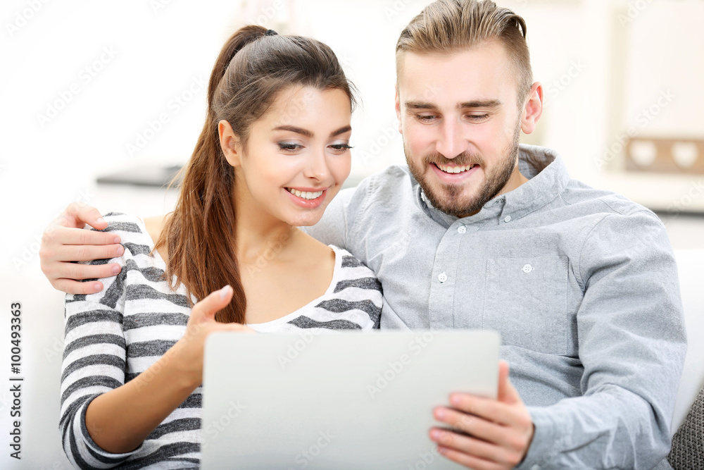 Happy couple sitting on sofa and working on a laptop