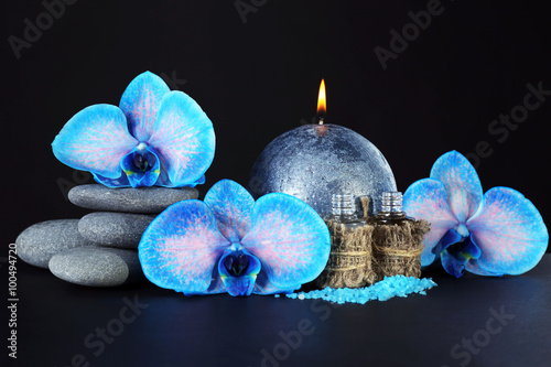 Fototapeta Naklejka Na Ścianę i Meble -  Spa set. Beautiful blue orchid with pile of pebbles, candle, sea salt and aroma oil on black background