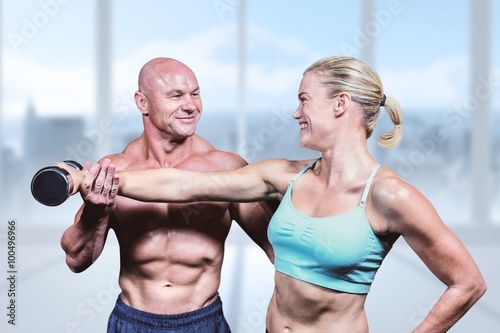 Cheerful trainer helping woman for lifting dumbbell