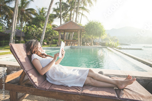 woman relaxing next to the pool and using tablet © Odua Images