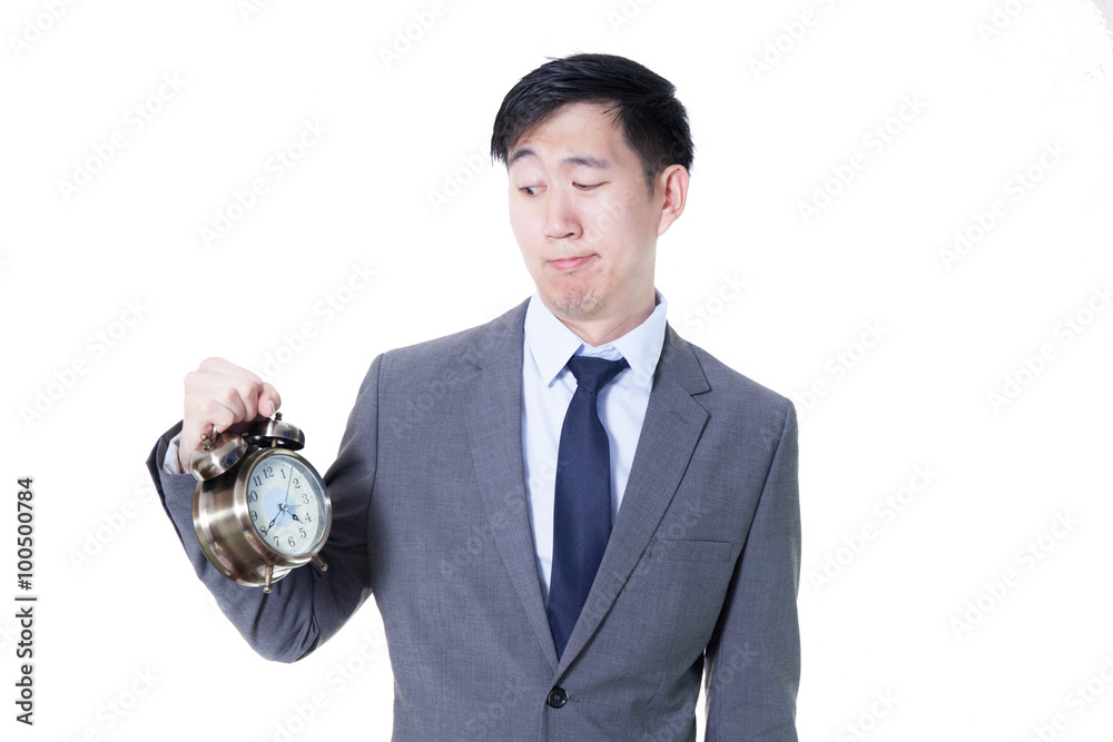Young Asian businessman holding a clock in unpleasant face expression - time and business concept Young Asian businessman holding a clock in unpleasant face expression - time and business concept