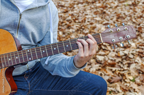 Young man playing guitar close up outdoors in autumn park