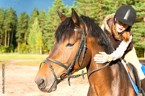 Girl equestrian riding horseback and stroking horse neck. Summer