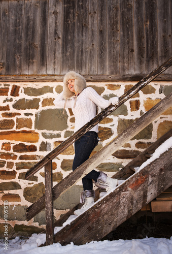 Cheerful woman in white sweater on stairs of cosy mountain house © Alliance