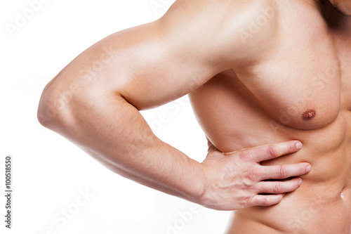 Muscular young man holding his back in pain, isolated on white b