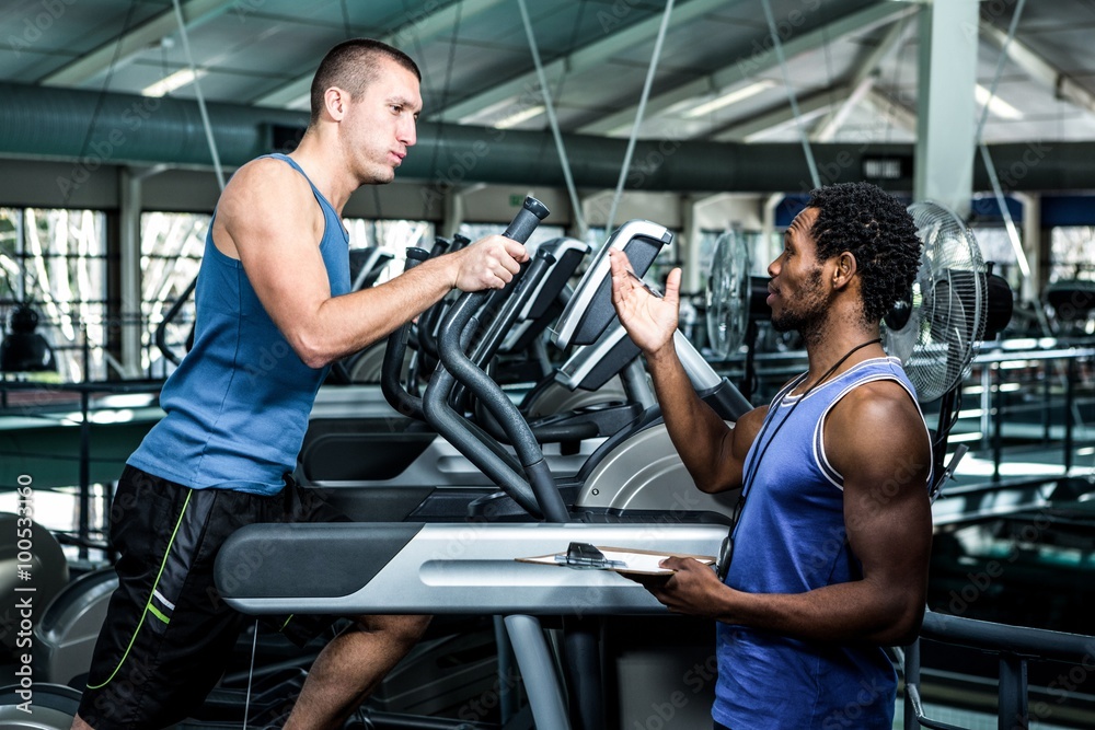 Muscular man using elliptical machine with trainer Muscular man using elliptical machine with trainer