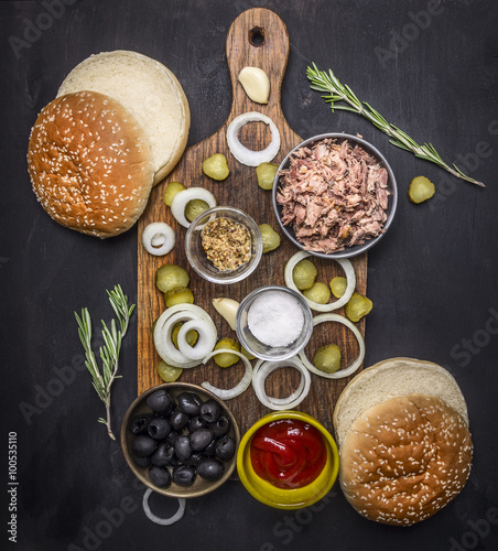 Ingredients for home kuking burger with tuna, pickled cucumbers, onions, olives and sauce on a cutting board on wooden rustic background top view close up