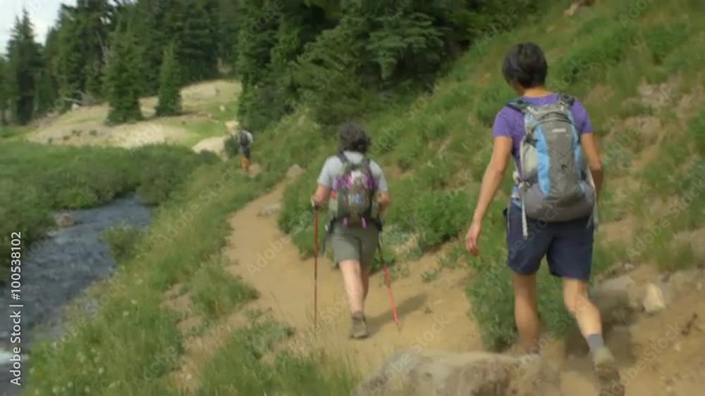 Camera follows two hikers as they walk on a trail by a stream Camera follows two hikers as they walk on a trail by a stream