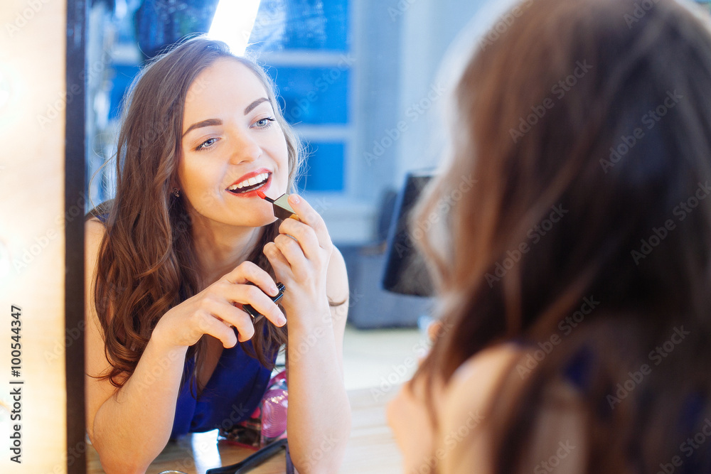 Young woman applying lipstick in front of a mirror Young woman applying lipstick in front of a mirror