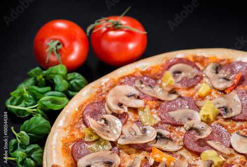 closeup Tasty pizza with tomatoes, cheese, basil and ham on a black background (shallow DOF)