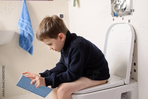 Boy sitting on the toilet and reading a book photo