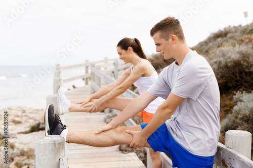 Runners. Young couple exercising and stertching on beach