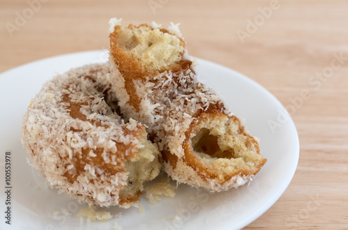 Plain coconut flake donut broken on plate