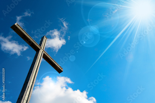 Christian Cross Against a Blue Sky / Wooden christian cross on blue sky with clouds and sun rays photo