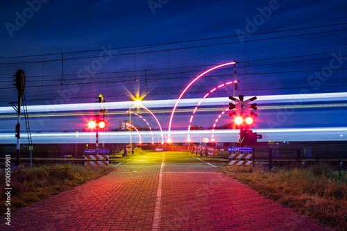 Bewaakte spoorwegovergang met brandende lichten in de nacht en voorbijrijdende trein