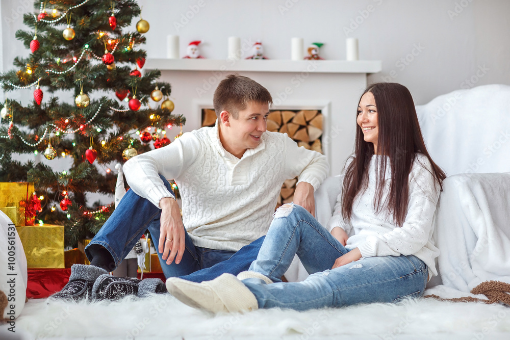 Young beautiful couple playing near a Christmas tree. Loving couple sitting by the fireplace. Young beautiful couple playing near a Christmas tree. Loving couple sitting by the fireplace.