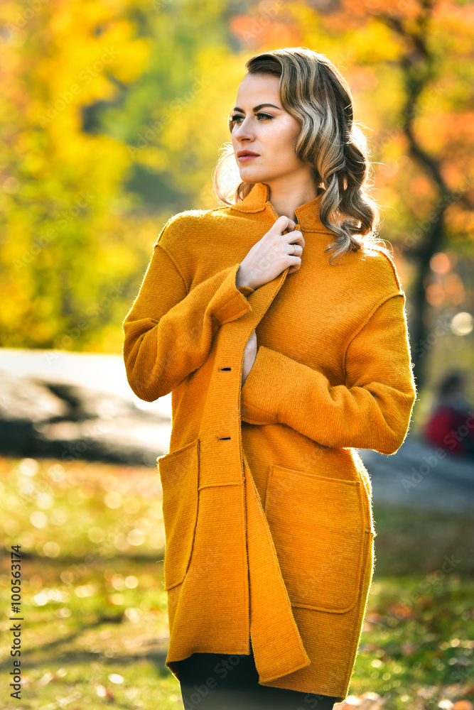 Beautiful young blonde model in elegant autumn coat standing in a park.