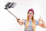 Happy girl in cap and glasses making photo by selfie stick and t