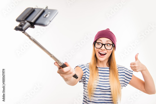 Happy girl in cap and glasses making photo by selfie stick and t