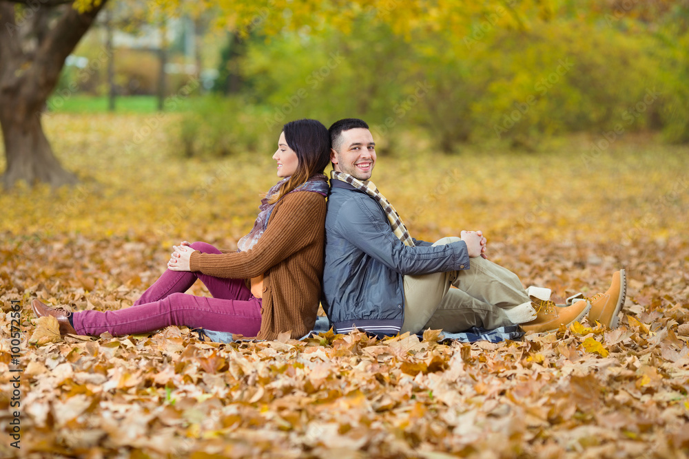 Happy young couple sitting back to back among autumn leaves Happy young couple sitting back to back among autumn leaves