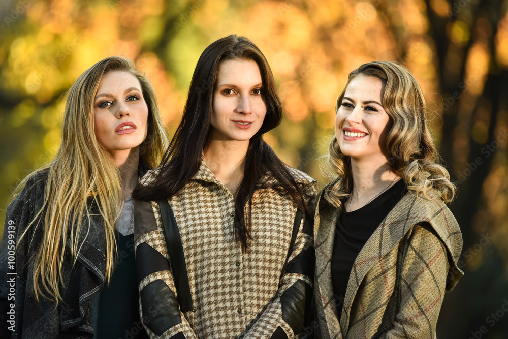 Three beautiful young fashion models posing against the backdrop of the autumn park.