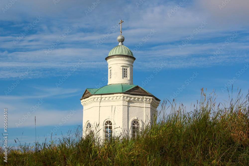 The old Russian stone chapel covered white paint and green roof on a background of green grass and blue sky with clouds. Secluded Orthodox Christian Church in the North island of white sea.