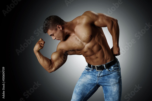 Handsome muscular man in blue jeans, showing his biceps. Silver tone.