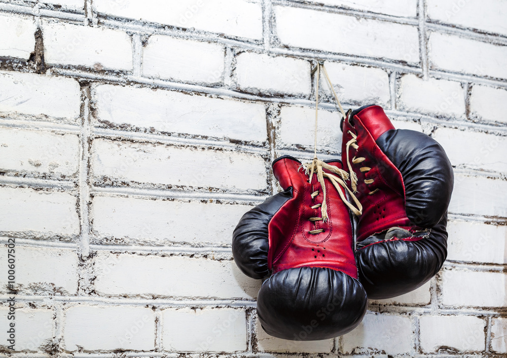 A pair of old boxing gloves hanging on white brick wall background.