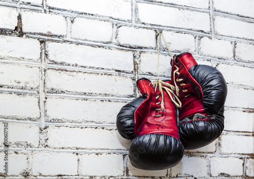 A pair of old boxing gloves hanging on white brick wall background. © Veresovich