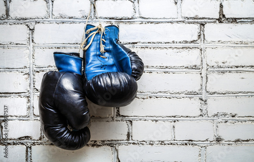 Pair of old blue boxing gloves hanging on white brick wall background. © Veresovich