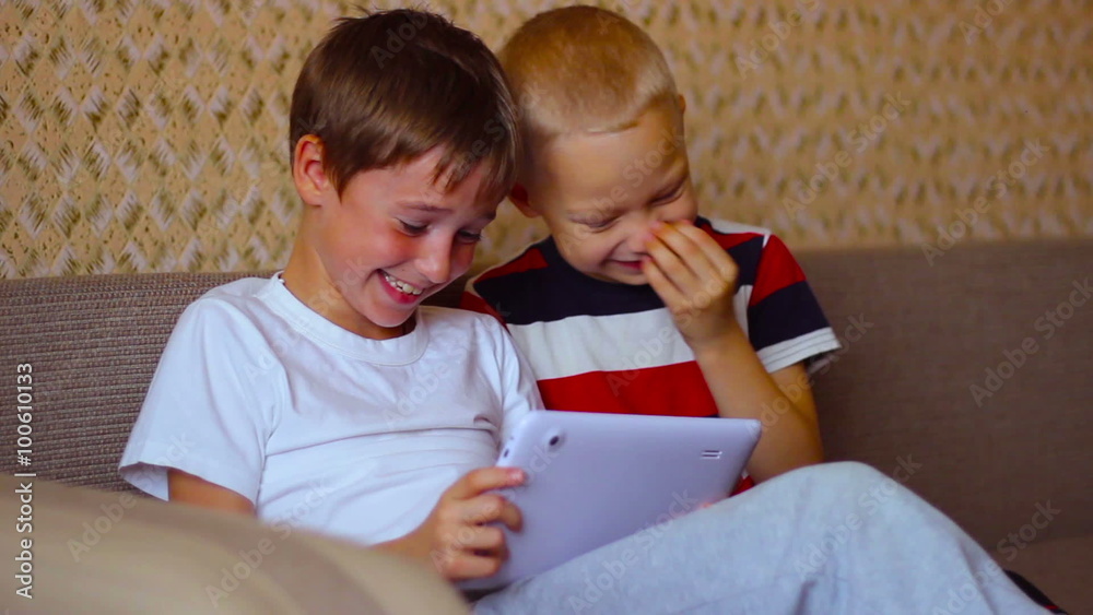 Two boys play on a white plate sitting on the couch Two boys play on a white plate sitting on the couch