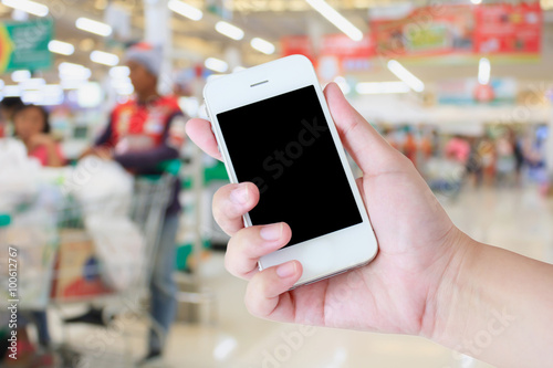 Hand holding mobile phone at supermarket checkout background