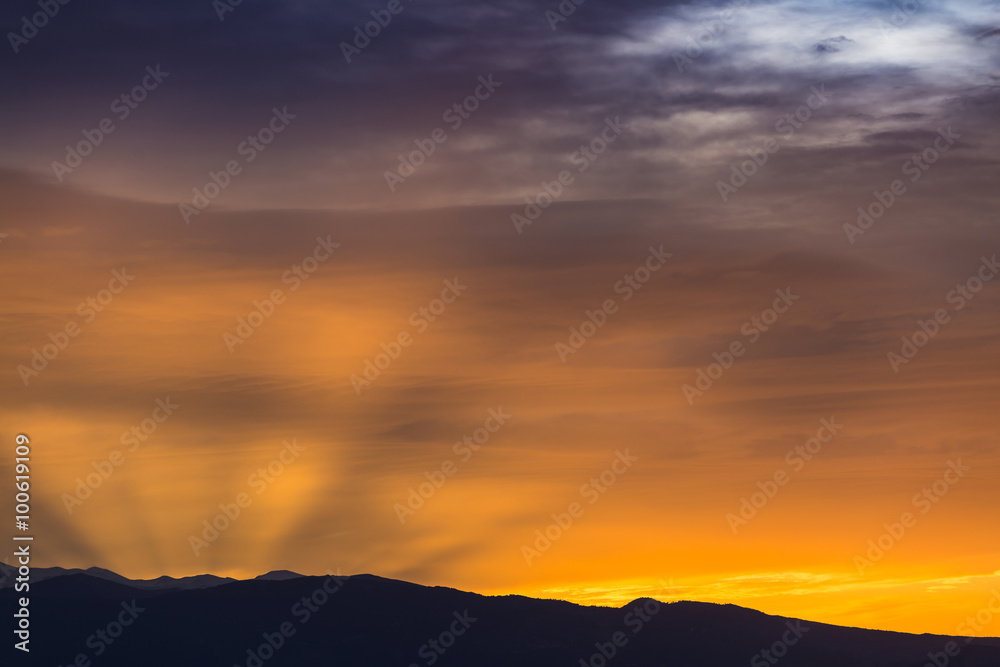 Sun behind dark mountain silhouettes, with colorful sky and clouds