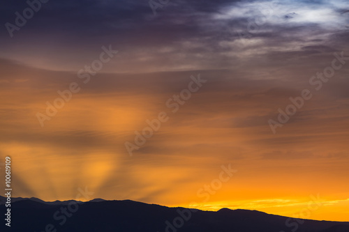 Sun behind dark mountain silhouettes  with colorful sky and clouds