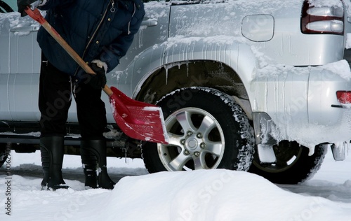 Man shoveling snow from his car wheels