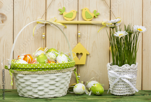 Easter decorations - flowers and basket with eggs on the wooden background.