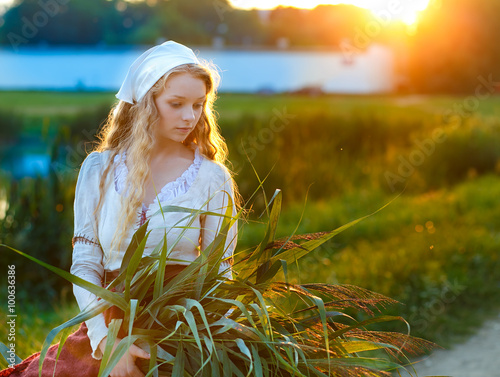 Fényképezés Young peasant woman with corn leaves at sunset