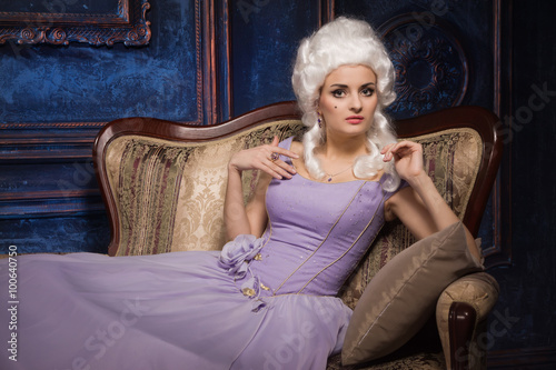 Woman in historic baroque style dress and white wig on the couc