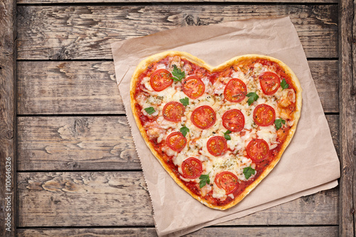 Heart shaped pizza margherita with tomatoes and mozzarella for Valentines Day on vintage wooden background. Food concept of romantic love.