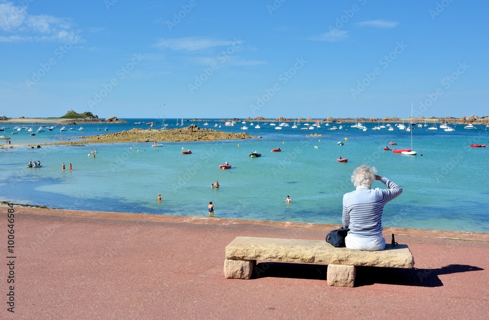 Une femme retraitée assise sur un banc de pierre regarde un beau paysage de mer