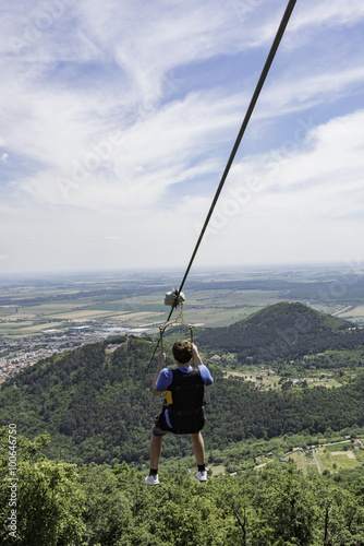Teen going on a zip line adventure above a valley. Teen boy going on a zip line adventure above a valley. Forest lay below and in the distance there are cultivated fields.