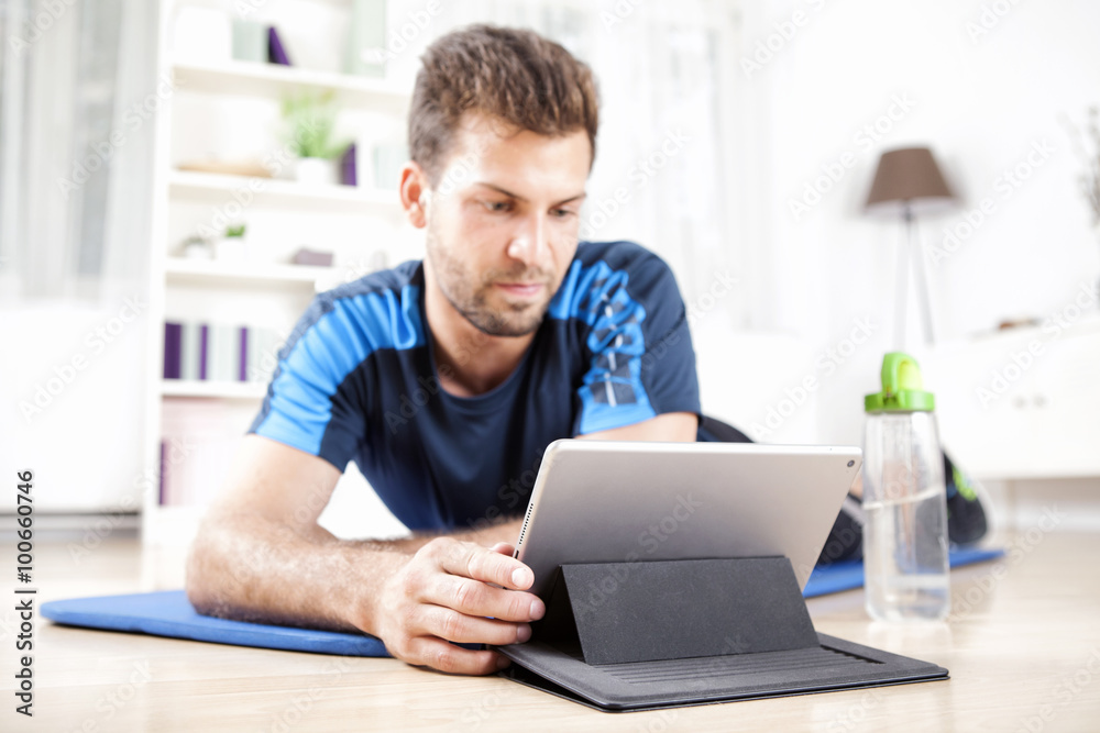 Man Lying on Exercise Mat While Using his Tablet Man Lying on Exercise Mat While Using his Tablet