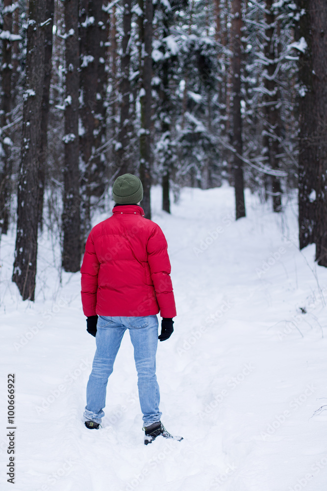 A man in a red jacket, walking in a snowy forest in the winter.