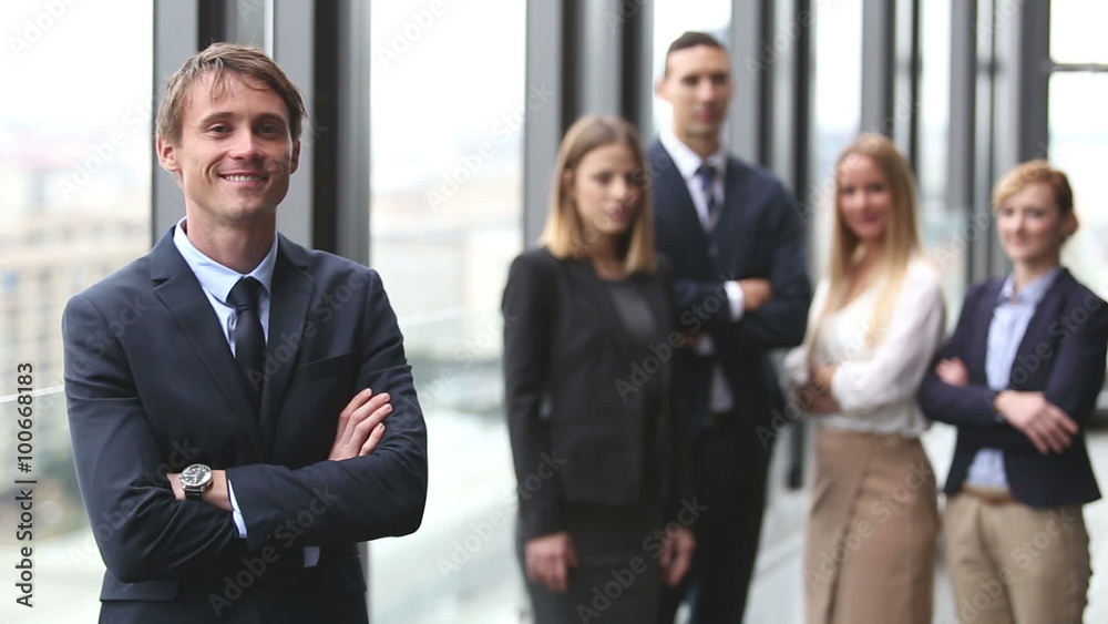 Portrait of handsome businessman smiling, colleagues in background Portrait of handsome businessman smiling, colleagues in background