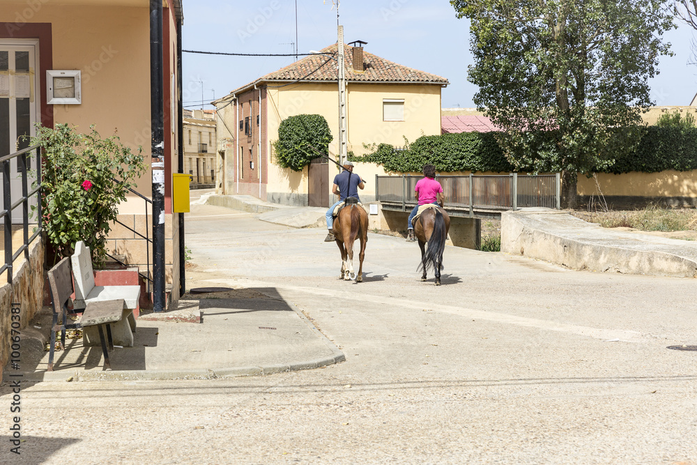 people riding horses on a town street - obrazy, fototapety, plakaty 