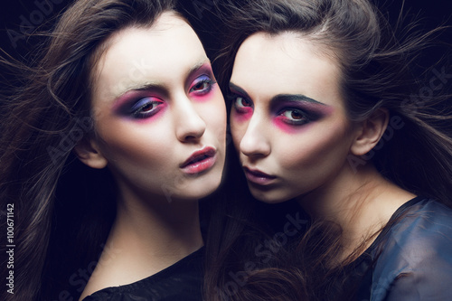 Portrait of two beautiful young girls twins in the studio with bright makeup on a black background, the concept of beauty