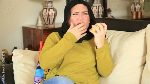 Muslim woman with a toothpain sitting on a sofa and eating pear photo