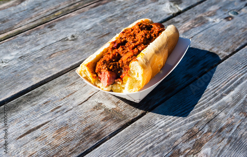 Partly eaten hot dog covered in chili on wood table