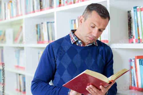 Obraz w ramie Man stood looking at book in library